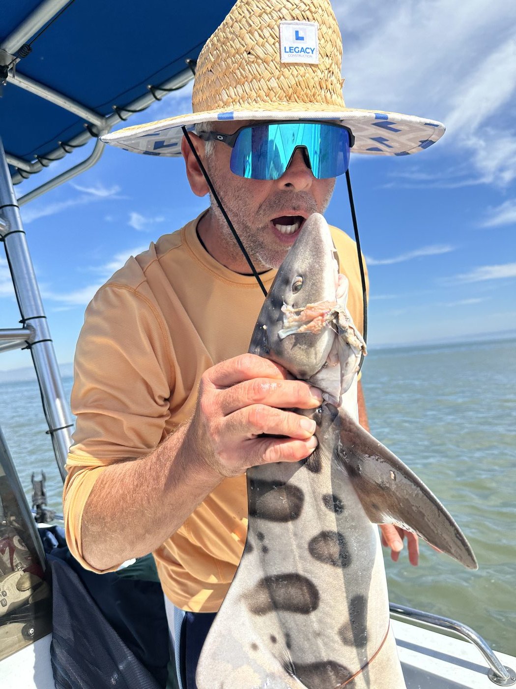 Billy Wills in a straw hat holding a small leopard shark on a boat
